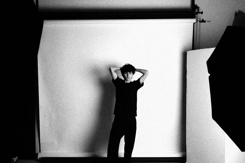 Wide view of Marcel standing with hands behind the head on a studio backdrop