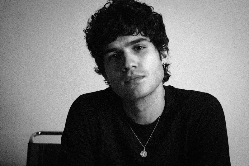 Pedro seated facing the camera with a pendant necklace over a dark shirt