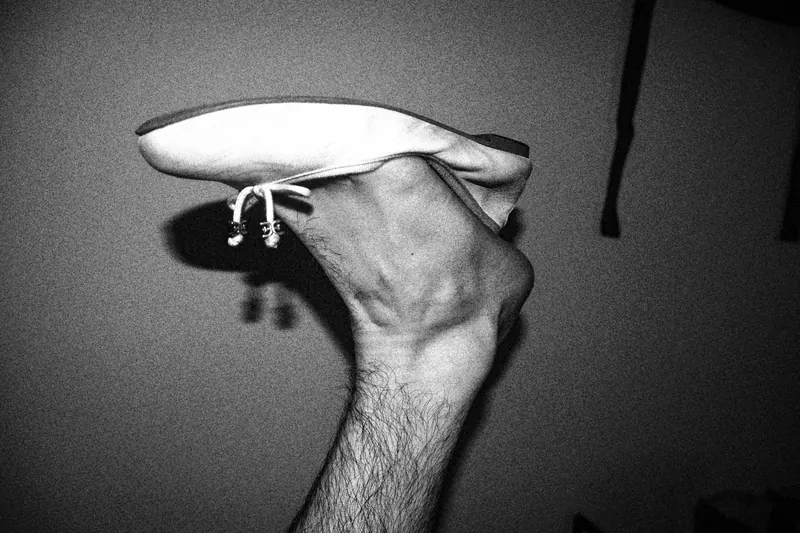 A hand holding a light canvas shoe with its sole facing upward