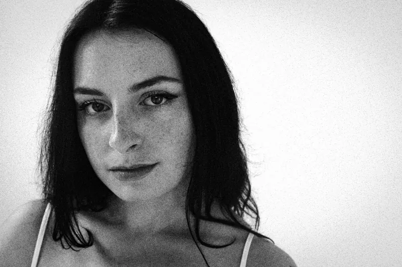 Magdalene facing the camera in a thin-strapped top against a light backdrop
