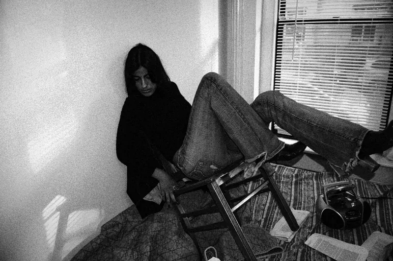 Vanessa seated by a window with legs raised over a folding chair