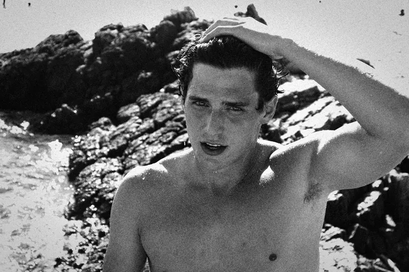 Charlie brushing a hand through wet hair on a rocky shore