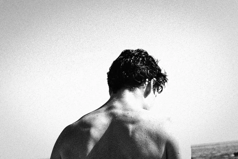 Charlie seen from behind, with bare shoulders against the sky and sea