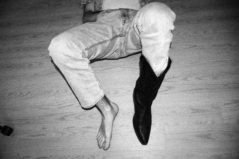 Overhead view of bent legs in light trousers, with one bare foot and one dark boot