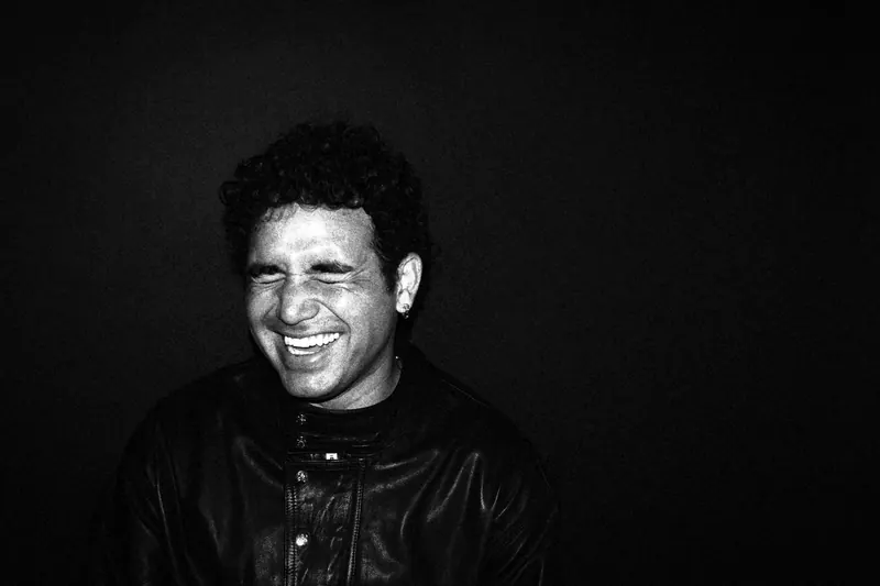 Marco laughing with eyes closed against a dark backdrop