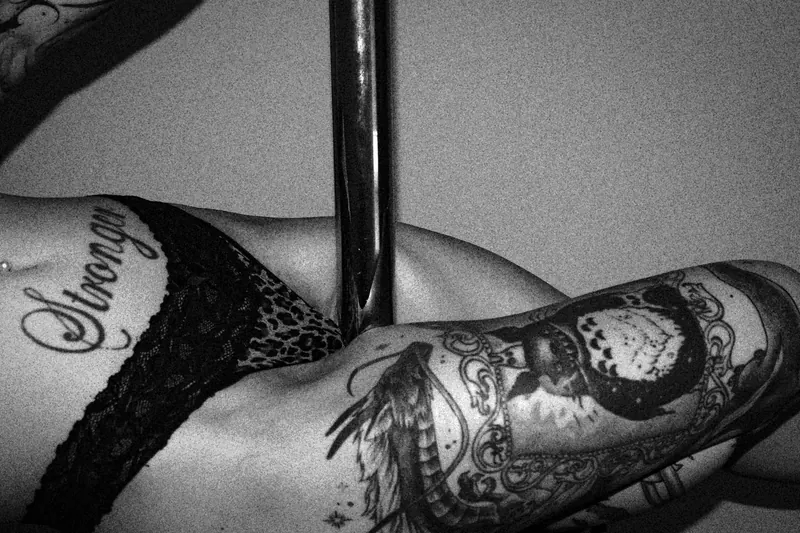 Close view of Gotho’s tattooed legs and black lace beside a pole