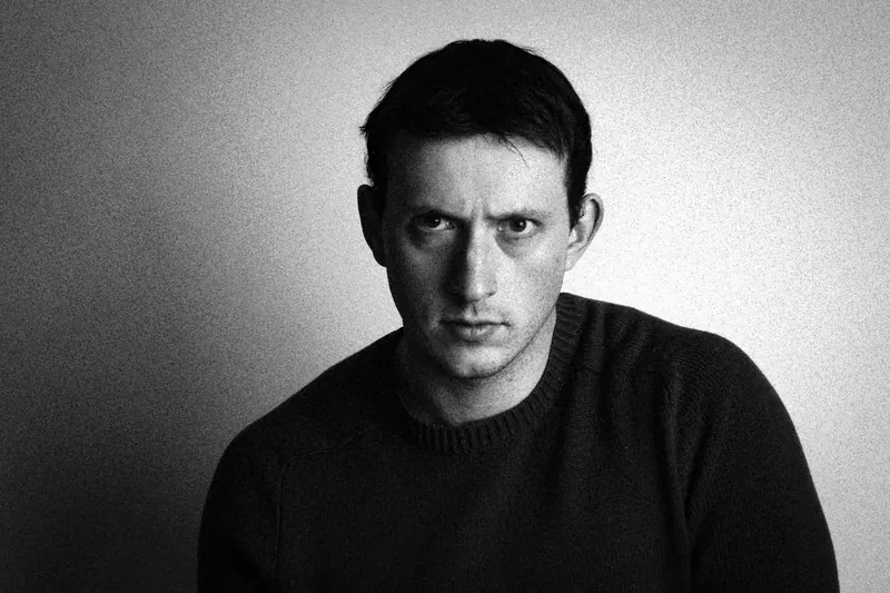 James leaning forward in a dark sweater against a light backdrop