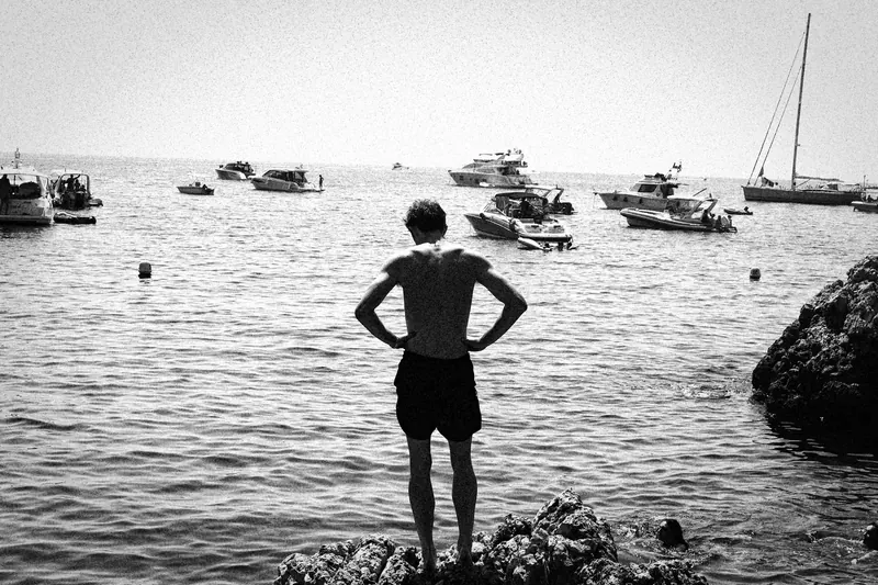 Max standing with hands on hips at the edge of a bay filled with boats