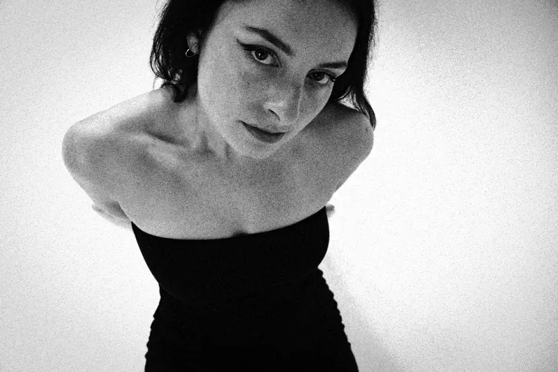 Magdalene looking up at the camera in a strapless dark dress