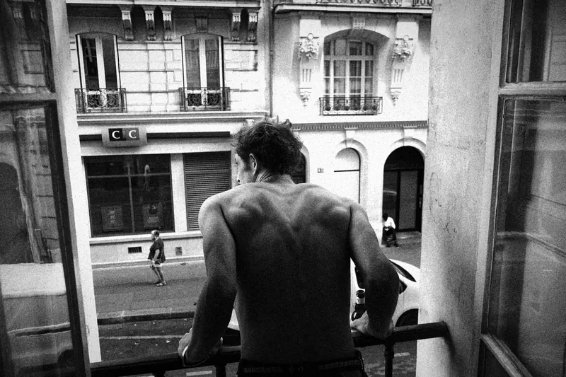 Max seen from behind leaning out of an open window toward the street