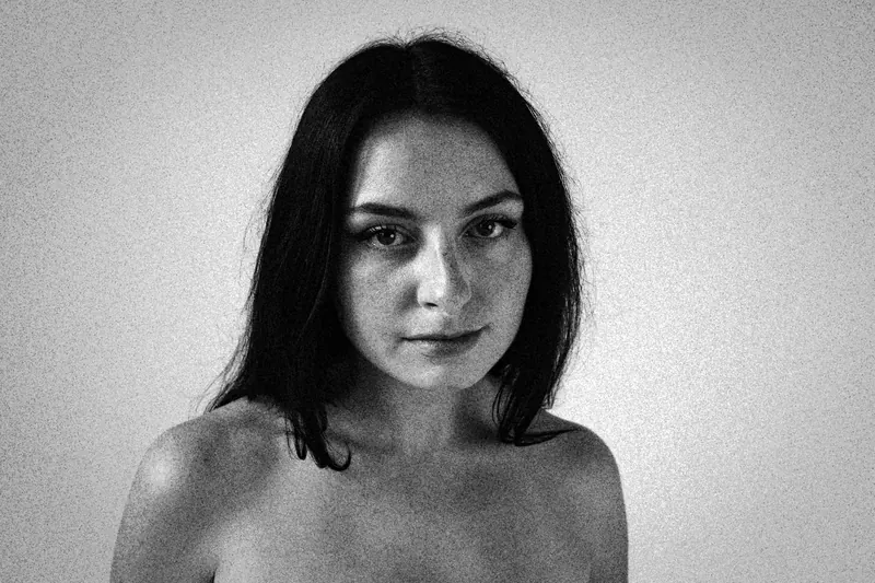 Magdalene with bare shoulders, facing the camera against a light wall